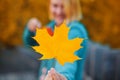 Blurred caucasian woman holding bright yellow maple leaf in hand. Autumn concept