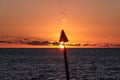 A blurred and de-focused silhouette of a gas torch with flame rising up against a setting sun.