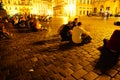 The blurred effect of long exposure movement of people sitting around a cobbled town square under golden glow of night lights
