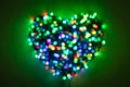 Blurred garland with multi-colored lights folded in the shape of a heart on a green background in dark Royalty Free Stock Photo