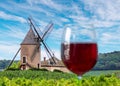 Blurred glass of red wine on foreground and the eponymous windmill of famous french red wine at the background. Romaneche-Thorins
