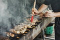 Blurred hands of man lubricates the meat with a sauce brush on long rectangular barbecue with smoke on the street outdoor. Royalty Free Stock Photo