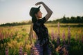 Blurred image of beautiful woman in hat posing among lupine flowers in sunset light in field Royalty Free Stock Photo