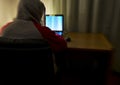 Blurred image from behind of an hacker with a sweatshirt and hood raised alone in his room using a laptop. for cyber security conc