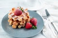 Blurred image of Belgian waffles with strawberries and powdered sugar on a plate and a cup of coffee on a light table