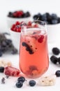Blurred image of a chilled fruit drink with ice and a sprig of lavender in the foreground, various berries in the background on a