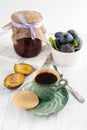 Blurred image of a cup of coffee, cookies and a jar of plum jam and plums in a bowl Royalty Free Stock Photo