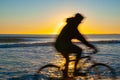 Blurred image of cyclist on beach back lit by sunrise on distant horizon