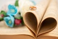 Blurred image of a heart made from book sheets with a ring and flowers in the background Royalty Free Stock Photo