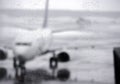 Blurred image of raindrops on terminal airport`s windows with white airplane