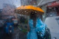 Blurred image, Image shot through raindrops falling on wet glass, abstract blur of lady with an yellow unbrella - monsoon stock