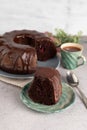 Blurred image of a slice of cake and a Bundt chocolate cake in the background, a cup of coffee on a light table Royalty Free Stock Photo