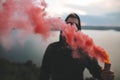 Blurred image of Ultras hooligan holding red smoke bomb in hand, standing on top of rock mountain with amazing view on river. Royalty Free Stock Photo