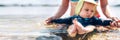 Blurred infant baby boy enjoying his swim in the sea, his mother`s hands are holding him. Focus on the baby`s feet Royalty Free Stock Photo