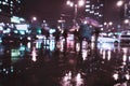 Blurred modern city at rayny night, defocused urban bokeh city lights, silhouettes of the walking people under umbrellas Royalty Free Stock Photo