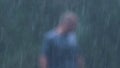 A blurred out, drenched man walks towards camera in a heavy rain storm.