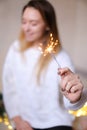 Blurred photo of young smiling woman sitting with bengal light near twinkling yellow garlands. Royalty Free Stock Photo