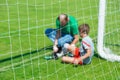 Blurred picture of a young injured male soccer or football player being treated by male team physician in front of the team goal