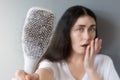 Blurred portrait of a shocked Caucasian young woman shows her hairbrush with losing hair. Gray background. The concept Royalty Free Stock Photo