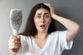 Blurred portrait of a shocked young woman shows her hairbrush with losing hair. Gray background. The concept of baldness Royalty Free Stock Photo