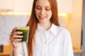 Blurred portrait shot of smiling attractive young woman holding glass with green vegetable detox smoothie cocktail from Royalty Free Stock Photo