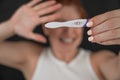 Blurred portrait of upset caucasian woman holding positive rapid pregnancy test on black background.
