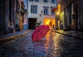 Blurred rainy city street at  evening pink umbrella on wet pavement medieval house street lamp blurred light Royalty Free Stock Photo