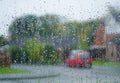 Blurred red car and housing estate seen through wet window with rain drops Royalty Free Stock Photo