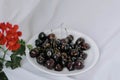 Blurred red geranium flower and fresh ripe dark black huge sweet cherries on white plate, light cloth blurred background Royalty Free Stock Photo