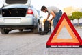 blurred scene of a young man changing a flat tire on the road, focus on hazard triangle Royalty Free Stock Photo