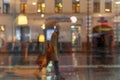 Blurred silhouette of an abstract unrecognizable girl with bags, view through a wet window with raindrops, city street in dark