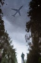 Blurred silhouette of reflection of one person walking alone on wet sidewalk of city park on rainy day. The plane flies across the Royalty Free Stock Photo