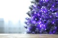 Blurred view of beautiful Christmas tree with purple lights near window indoors, focus on wooden table Royalty Free Stock Photo