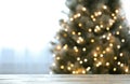 Blurred view of beautiful Christmas tree with lights near window indoors, focus on wooden table. Space for text Royalty Free Stock Photo