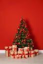 Decorated Christmas tree and gift boxes near red wall Royalty Free Stock Photo