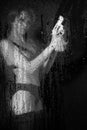 Blurred woman in lingerie and with a revolver in her hands behind wet glass with raindrops