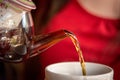 Blurred woman in red pouring tea from a glass teapot Royalty Free Stock Photo