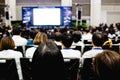 Blurry of auditorium for shareholders` meeting or seminar event with projector and white screen, many business people listening o