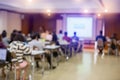 Blurry of auditorium for shareholders` meeting or seminar event with projector and white screen, many business people listening o