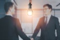 Blurry businessmen shaking hands together on abstract office interior background with glowing light bulb. Work ideas and