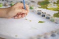 Blurry cropped photo of female hand painting with brush on paper, selective focus on acrylic paints in plastic boxes Royalty Free Stock Photo