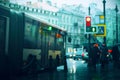 A blurry image of a city street with traffic lights and road signs, where people are walking, and next to the roadway goes a bus