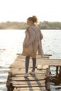 Blurry image of teenage girl wearing a beige coat and blue jeans standing near the water, overexposed shot.