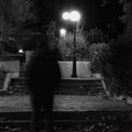 Blurry male figure walking in park with lampposts at night