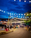 Blurry people hanging out at waterfront boardwalk string lights, beach chairs, patio restaurant dining tables sunset blue hour Royalty Free Stock Photo