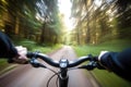 a blurry photo of a person riding a bike on a road in the woods with trees in the background and a person holding the handlebar Royalty Free Stock Photo