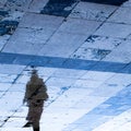 Blurry reflection shadow silhouette on wet city sidewalk of a mysterious person walking in the night