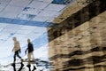 Blurry reflection shadow silhouettes of two young men walking on a vintage pavement on wet city street