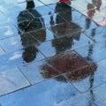 Blurry reflection shadows silhouettes of a woman under umbrella and a man walking in the rain in the city sidewalk Royalty Free Stock Photo