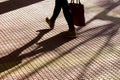 Blurry silhouette shadow of legs of a person carrying a bag while walking on tiled street sidewalk